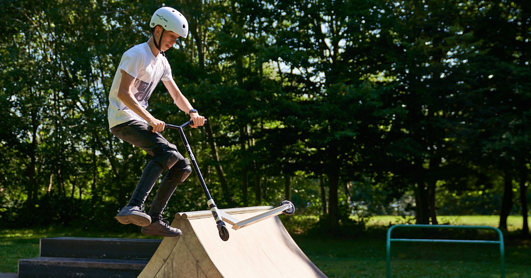 Teenage boy performing trick on a Zinc Stunt scooter in a skate park.