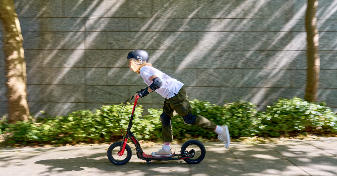 Big wheel scooter being used by teenage boy outside in an urban built up area.