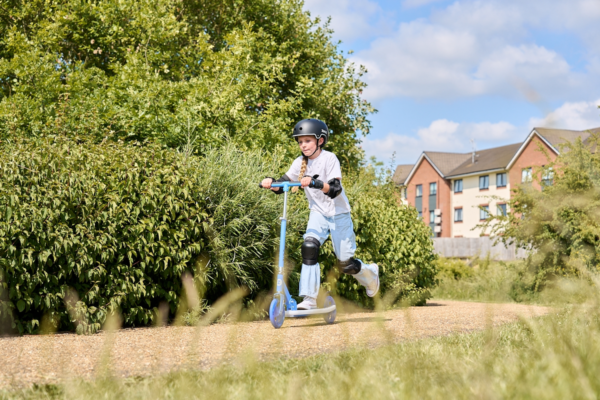 A child scooting on a Zinc Sports big wheel Moon scooter through a quiet path.