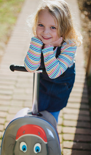 Girl leaning on her Flyte scooter suitcase featuring elephant design.