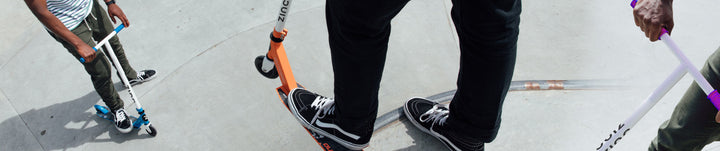 Close up of feet on a stunt scooter at a skate park.