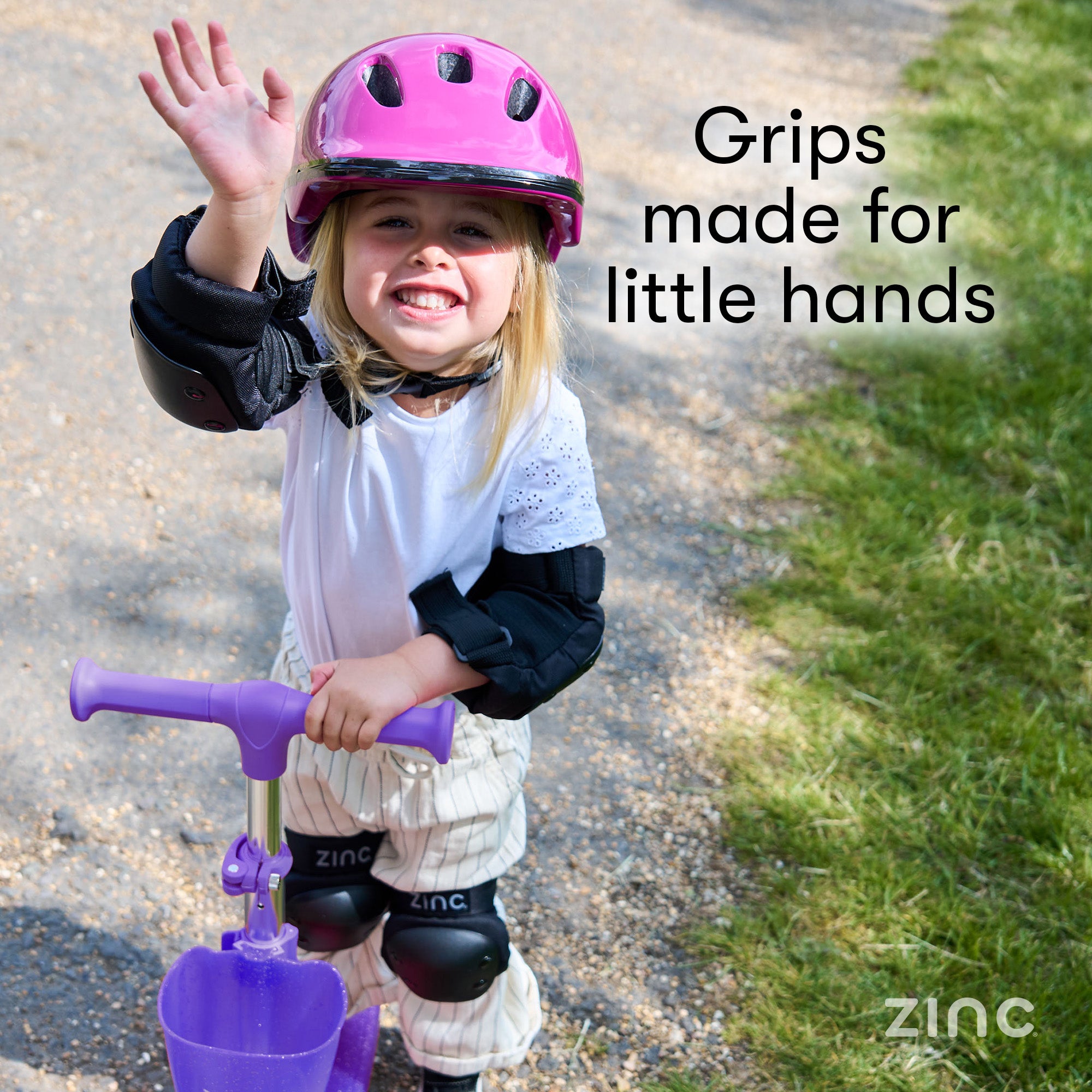 Child wearing safety gear and a pink helmet, standing on a path with 'Grips made for little hands' text and 'Zinc' branding.