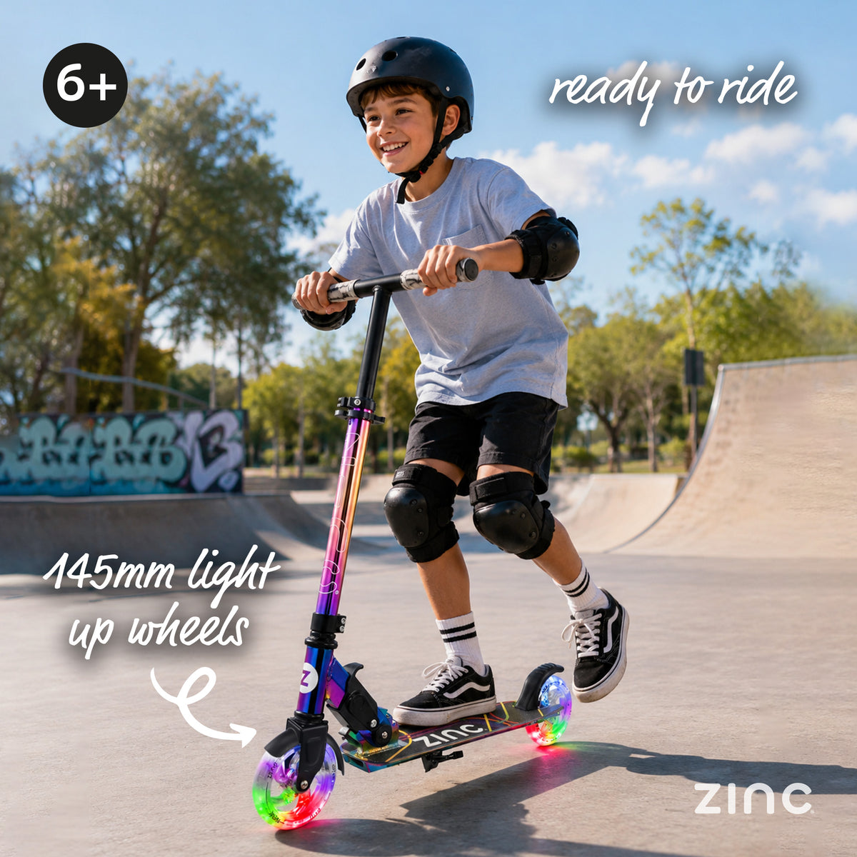 A child wearing a black helmet rides the Zinc neochrome scooter with glowing multicolour light-up wheels in an outdoor skatepark. Text overlays highlight the features: '145mm light up wheels' and 'ready to ride'.