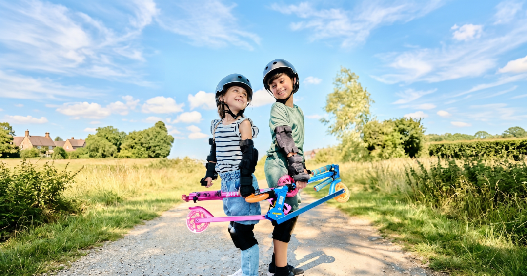 Two children stood outside with their Zinc Sports foldable two wheel scooters for kids. Wearing zinc scooter helmet and pads.