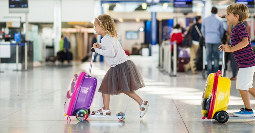 Zinc Scooter Suitcases in Pink and yellow being scooted through an airport by a little boy and little girl.
