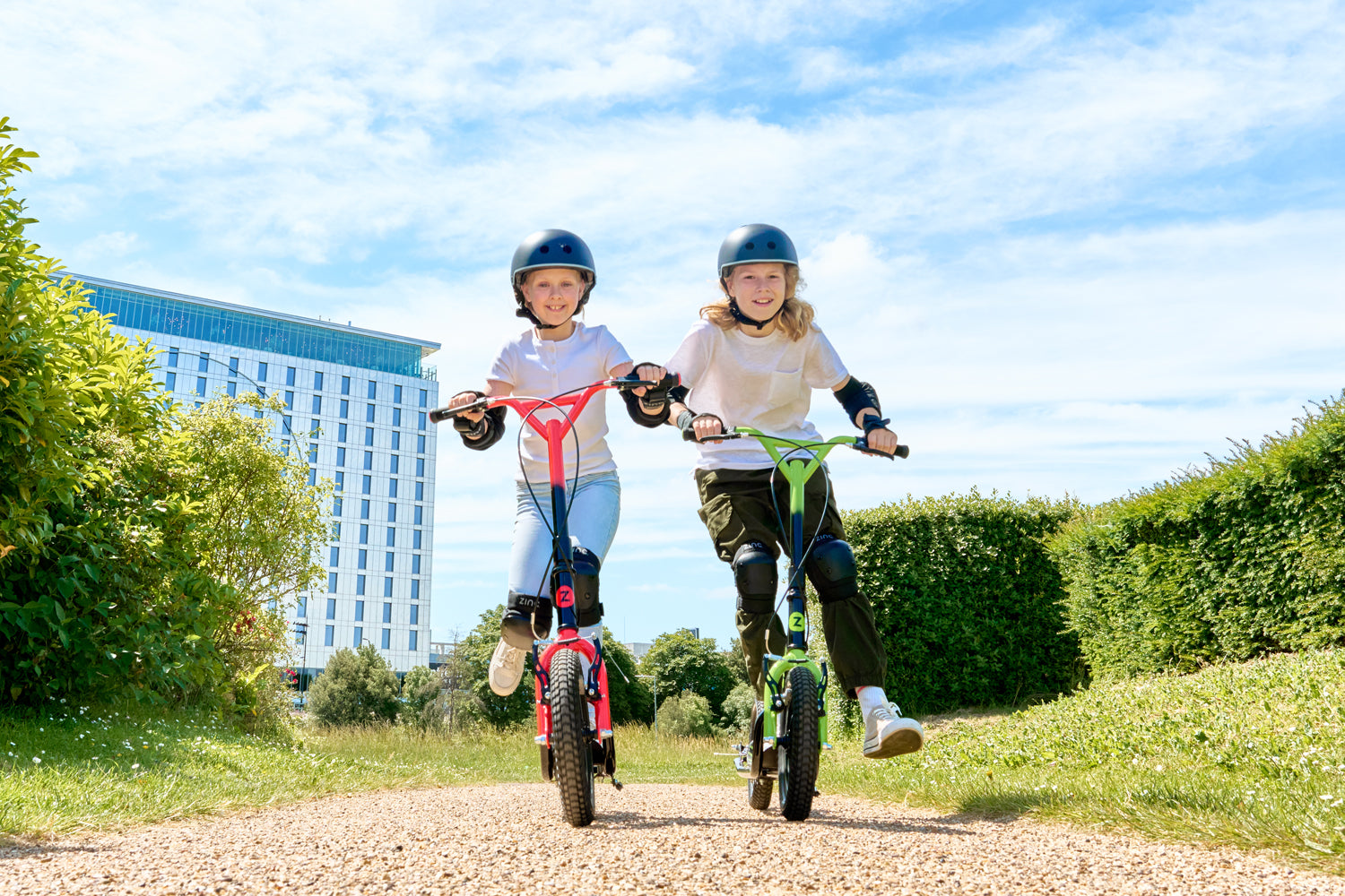 boy and girl riding their Zinc Radikal big wheel scooters outside in the sun.