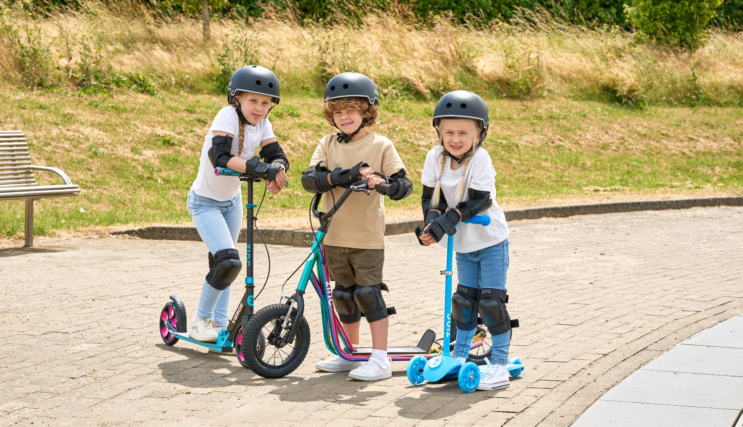 3 children on their Zinc scooters wearing helmets and full protective gear.