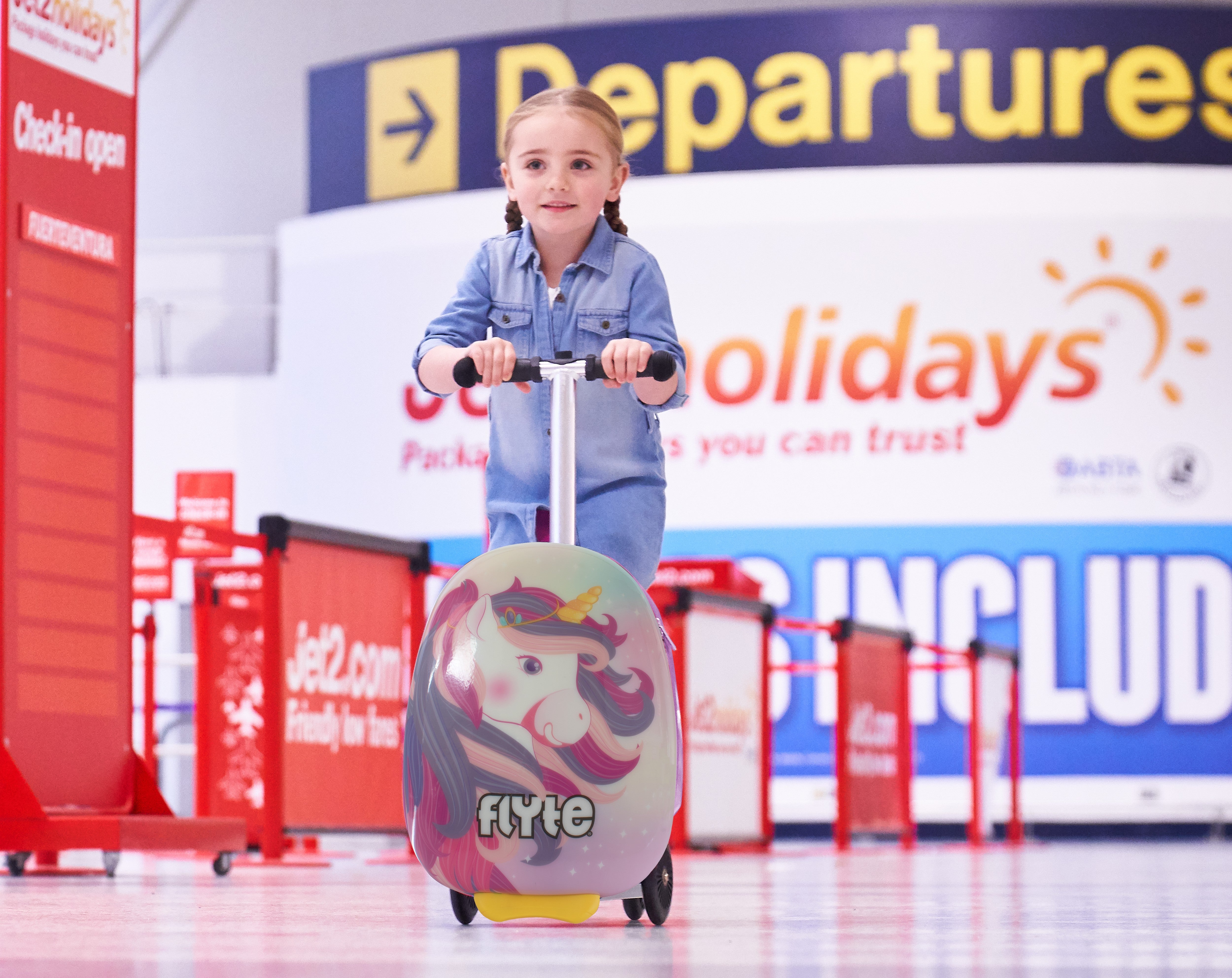 Little girl riding scootcase through the airport.