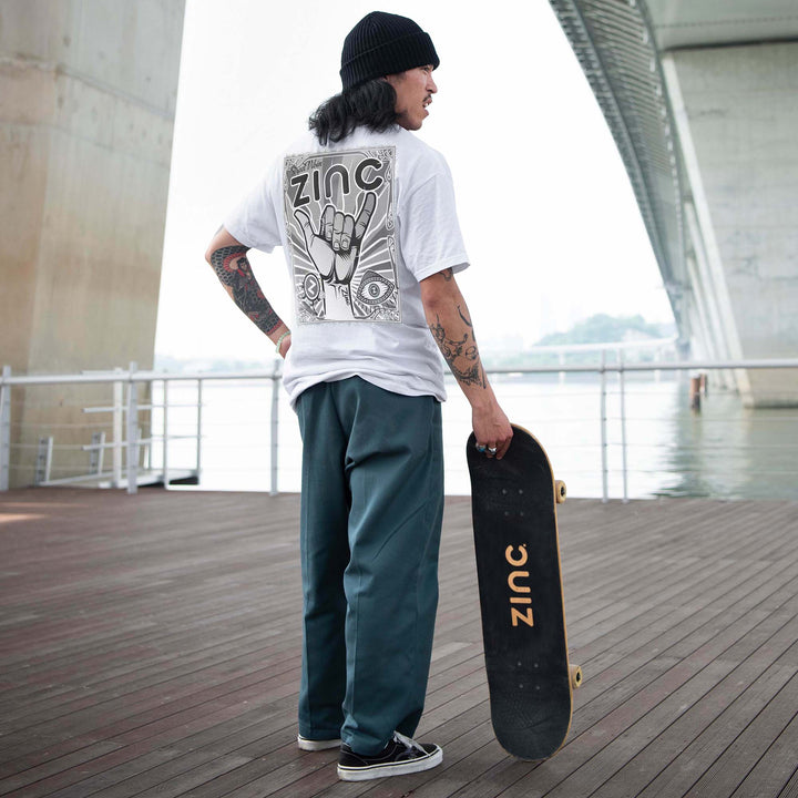 Skate boarded in a Zinc Black and White graphic T-shirt standing with his skateboard.