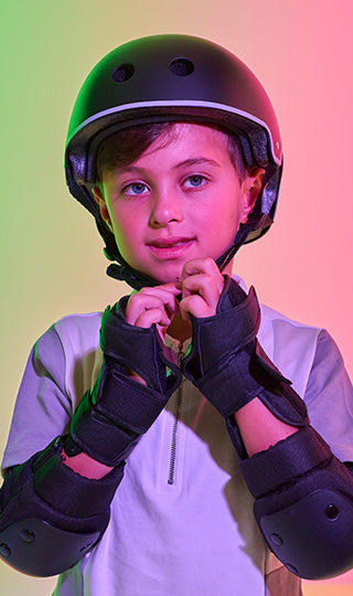 Boy securing his Zinc scooter helmet whilst wearing wrist and arm protection.