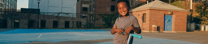 Boy in a playground smiling with his zinc scooter.