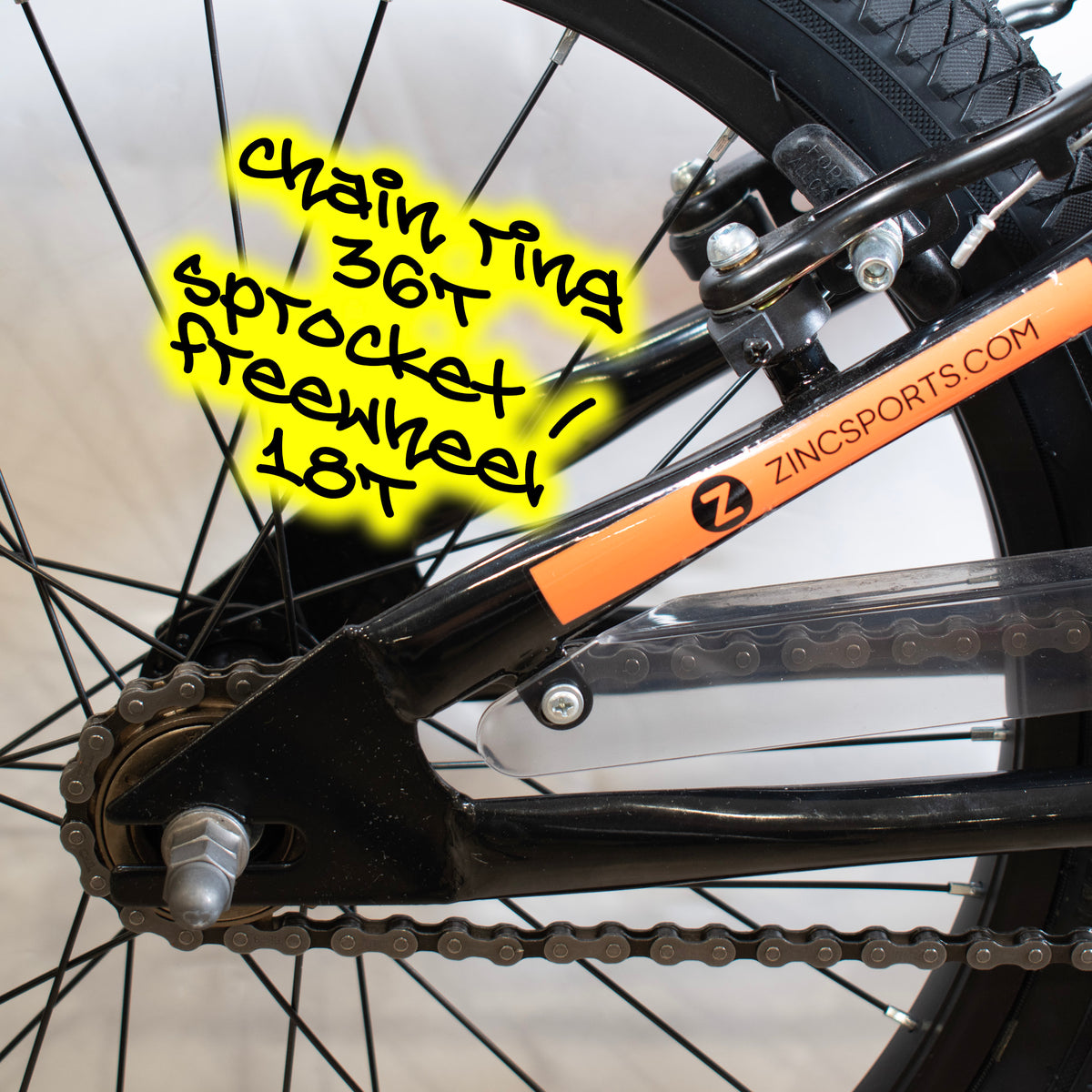 Close-up of a bicycle rear wheel and chainstay area with a bright orange frame sticker reading ZINCSPORTS.COM.