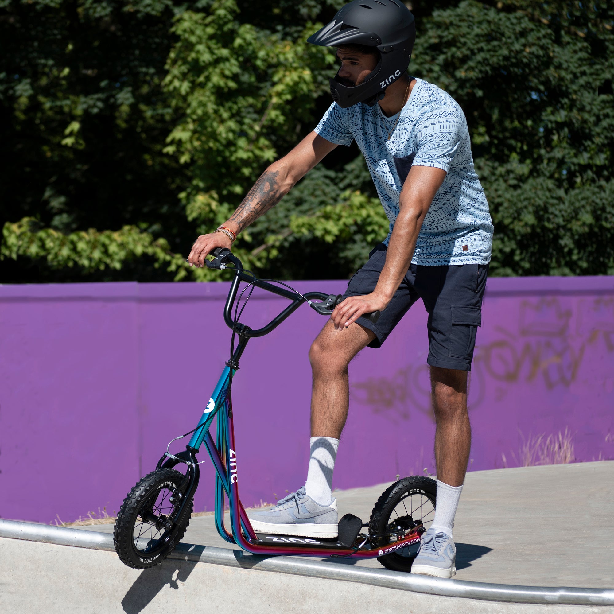Boy riding Zinc 12 Inch BMX Scooter Neochrome Multi-colour at Skate Park