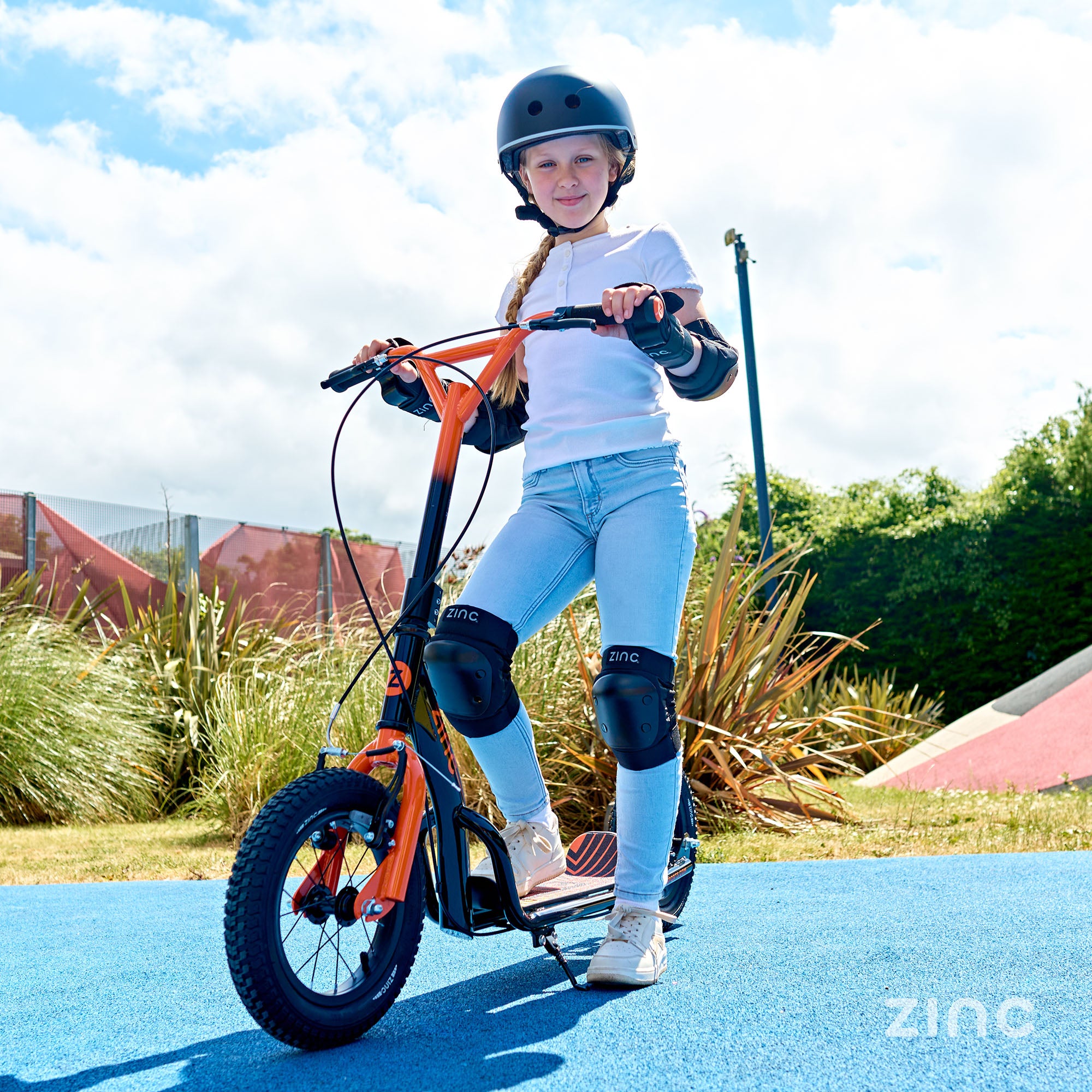 Zinc Radikal BMX Scooter in Orange being used by a girl in full protective gear