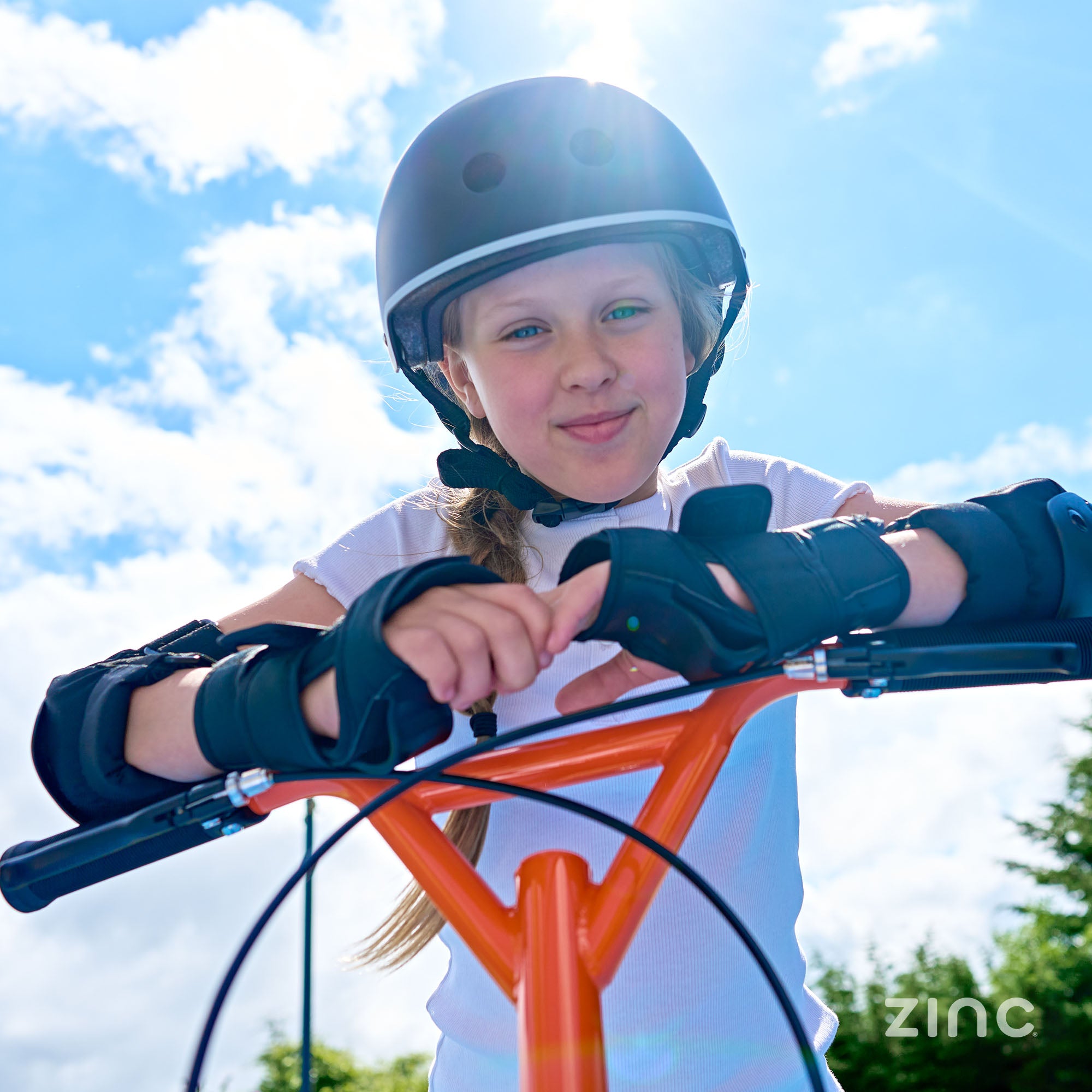 Close up of girl in helmet smiling while leaning on the handle bars of her Oranage Zinc Radikal scooter