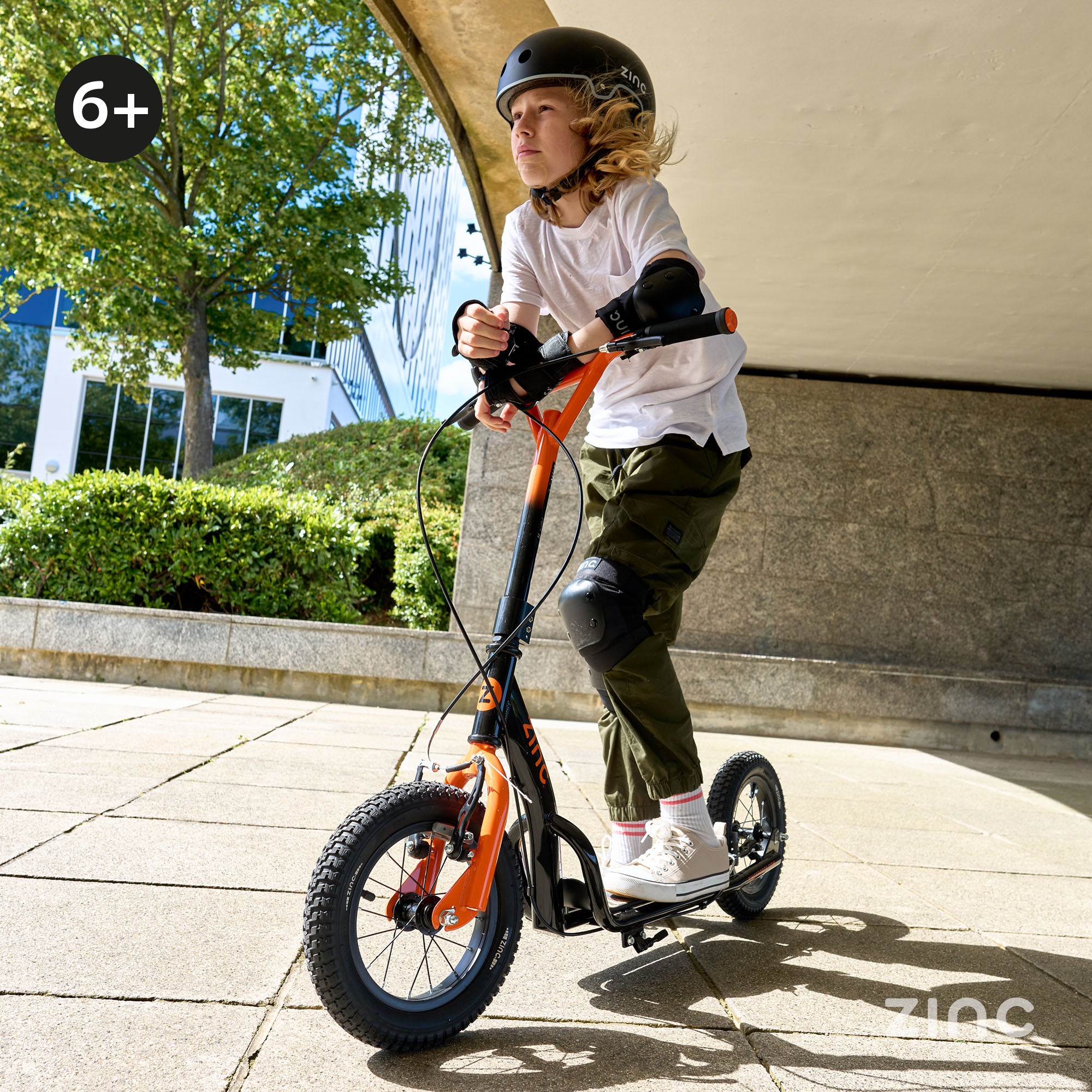Boy riding Zinc Radikal 12 inch BMX scooter wearing safety helmet and protective pads
