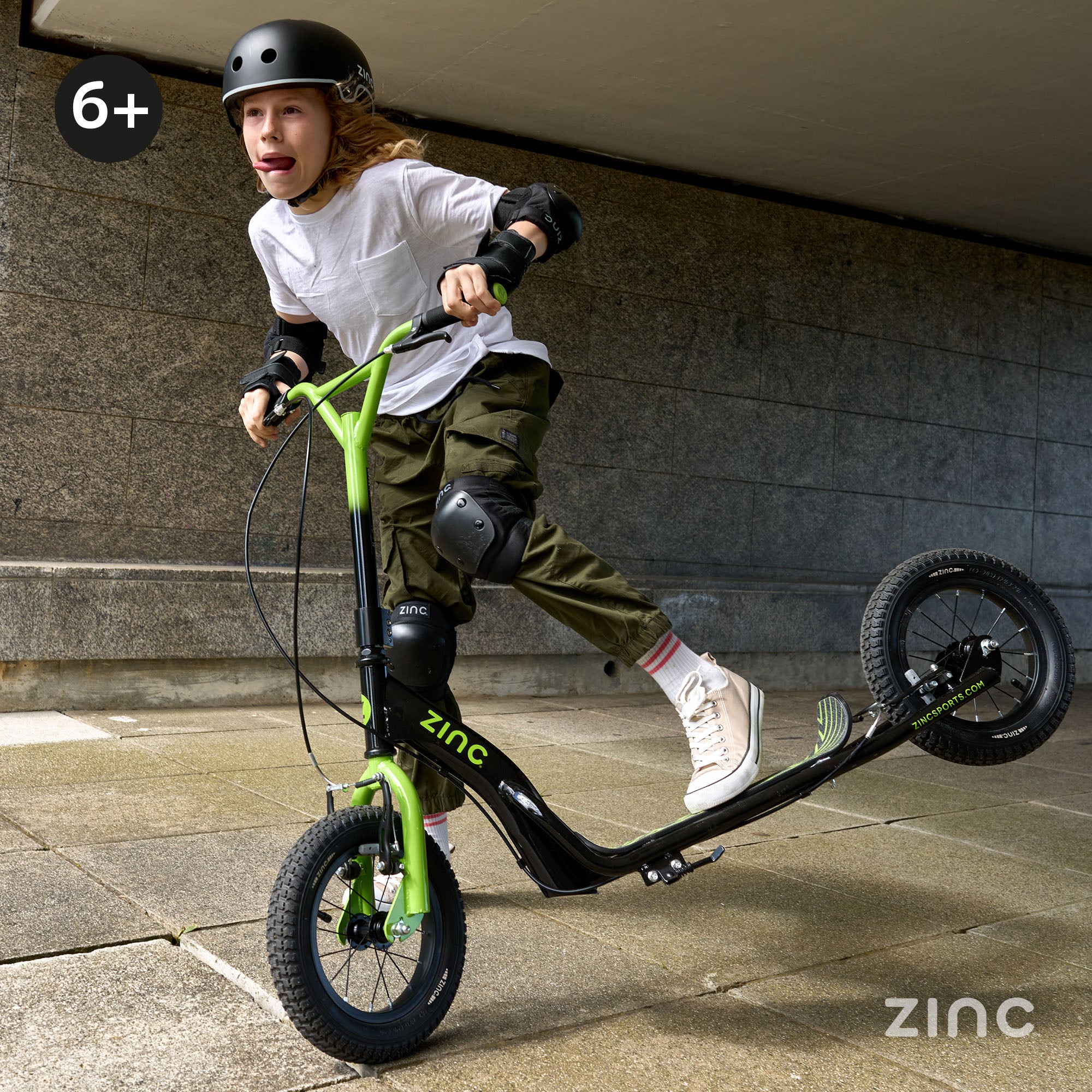 Young rider doing BMX tricks on green Zinc Radikal 12 inch big wheel scooter