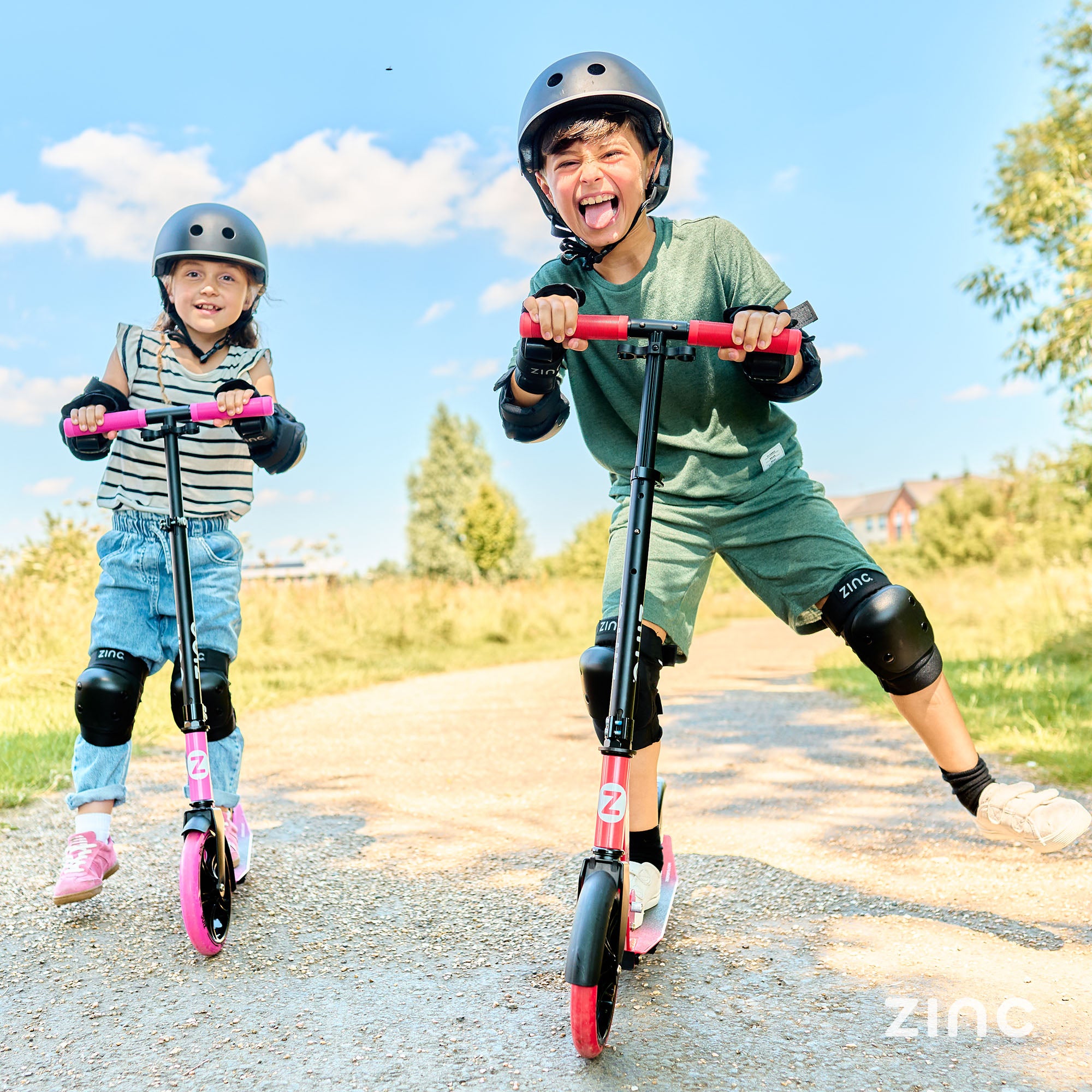 2 children riding zinc scooters in pink and red while wearing helmets and protective pads