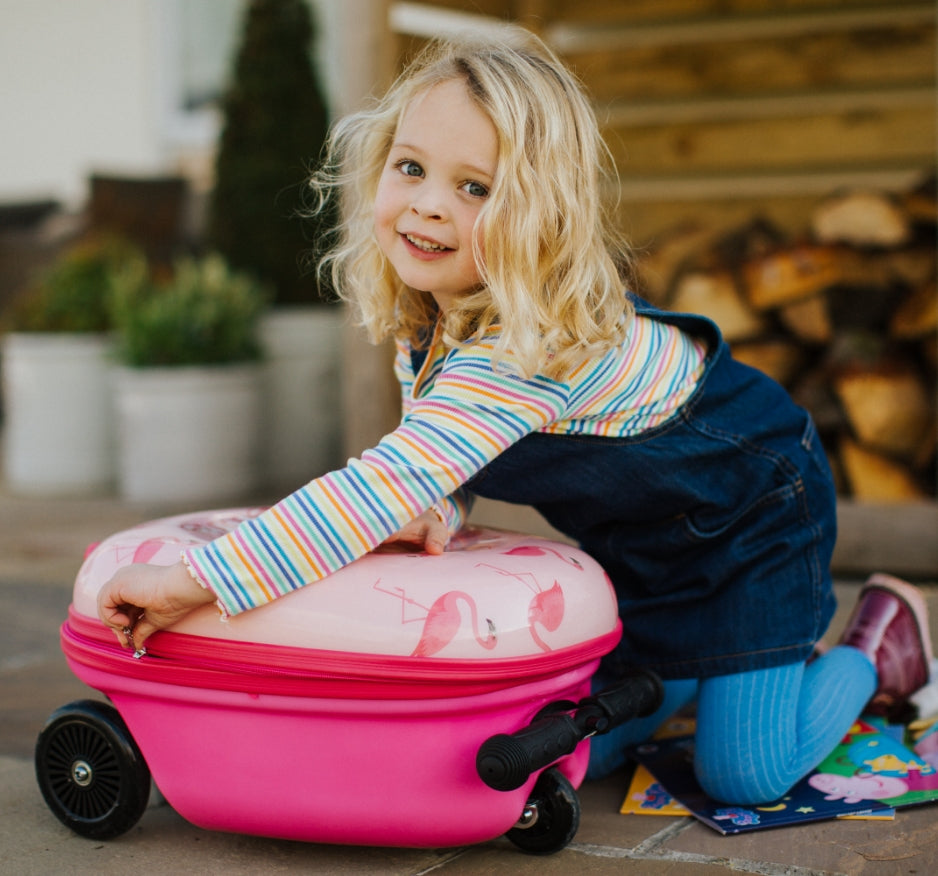 Little girl zipping up her Flyte scooter suitcase featuring flamingo design.