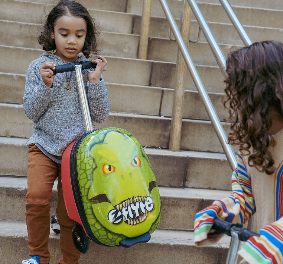 Boy carrying his Darwin the Dinosaur scooter suitcase down the stairs.