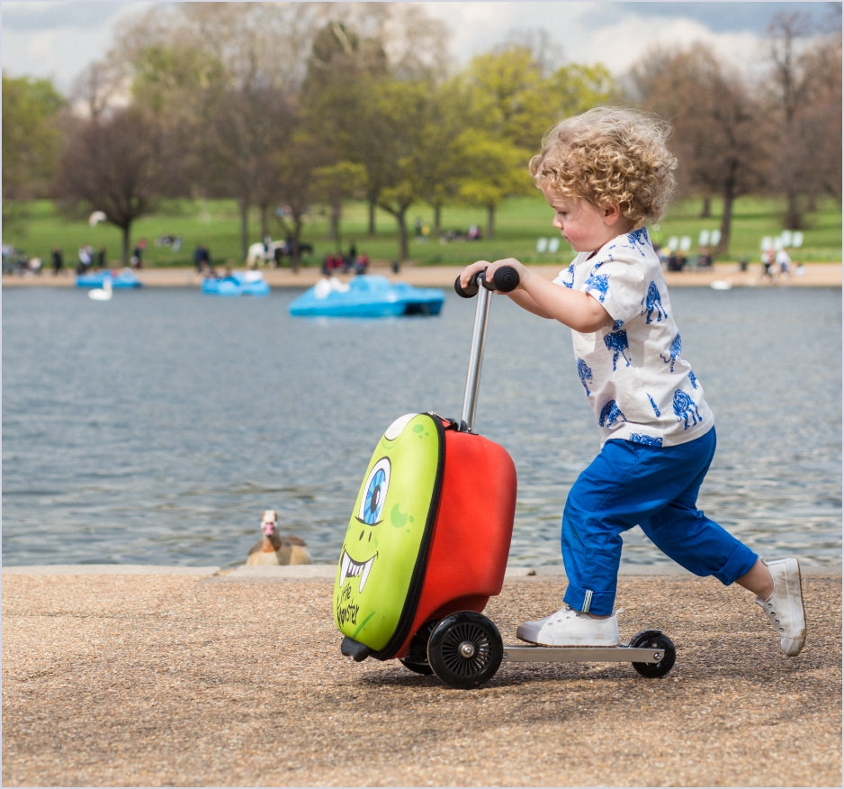 Boy scooting on Zinc Flyte monster design scooter suitcase next to a lake.