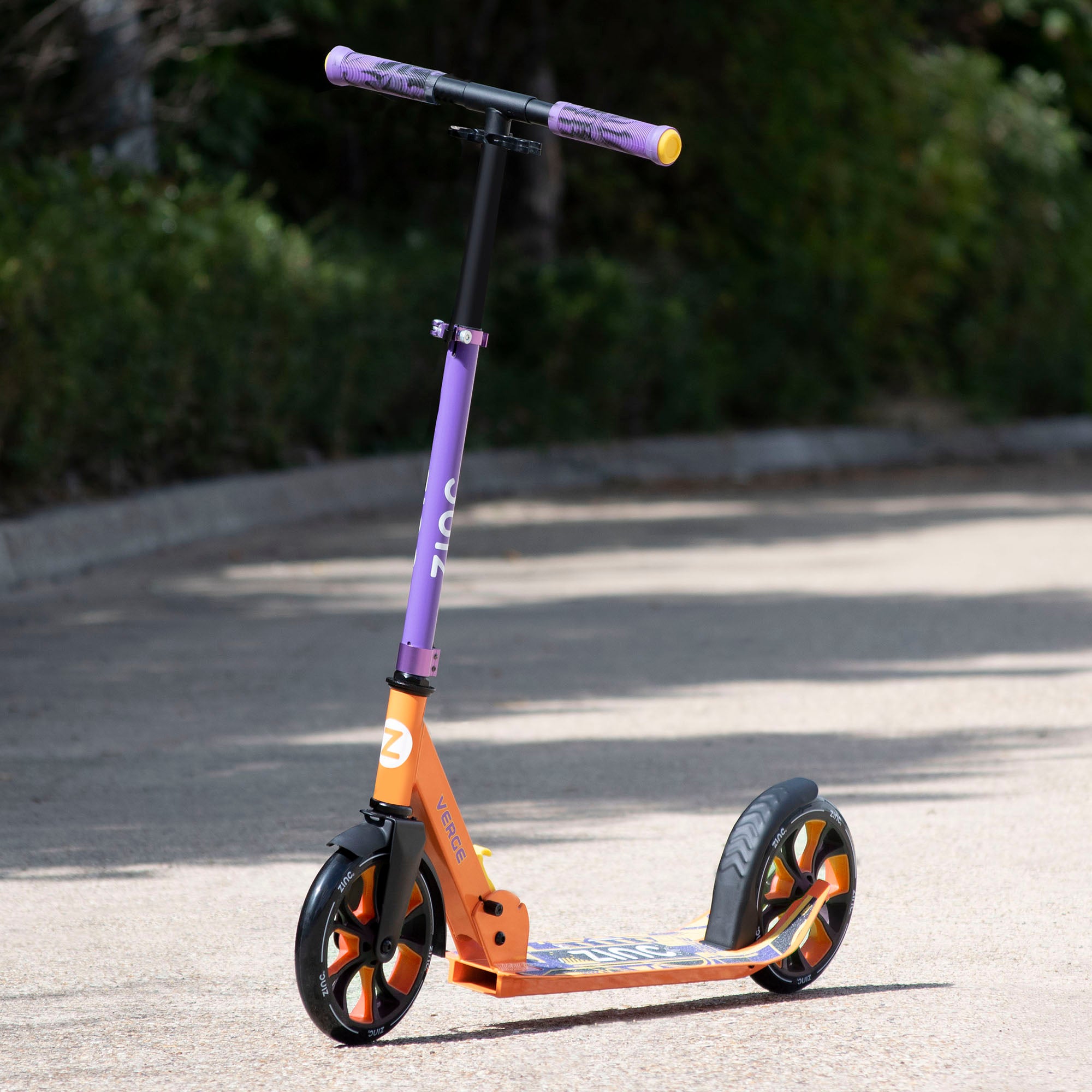 A folding scooter with orange deck, black wheels and purple handlebar, placed on a pathway.